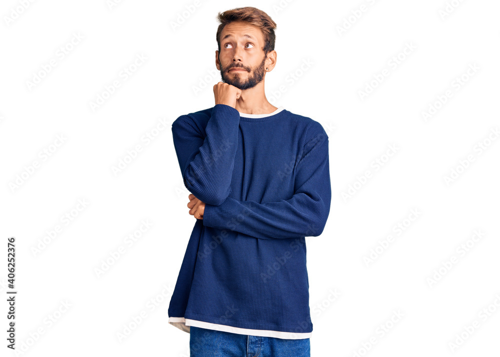 Handsome blond man with beard wearing casual sweater with hand on chin thinking about question, pensive expression. smiling and thoughtful face. doubt concept. Handsome blond man with beard wearing casual sweater with hand on chin thinking about question, pensive expression. smiling and thoughtful face. doubt concept.