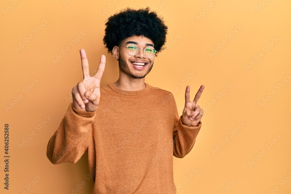 Young african american man with afro hair wearing casual winter sweater smiling looking to the camera showing fingers doing victory sign. number two. Young african american man with afro hair wearing casual winter sweater smiling looking to the camera showing fingers doing victory sign. number two.