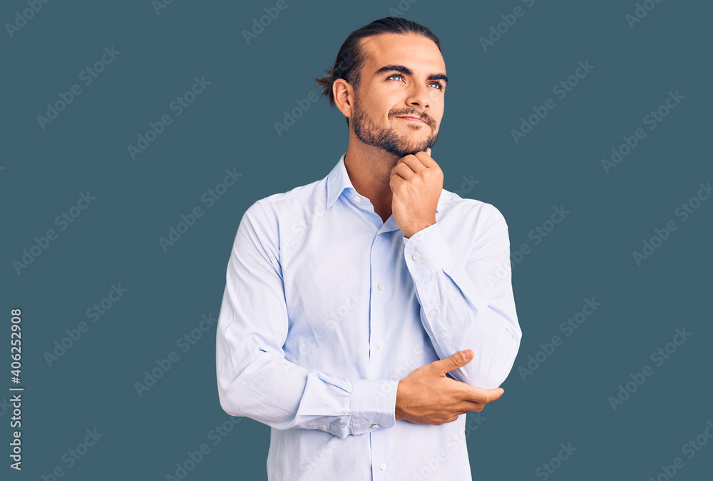 Young handsome man wearing business clothes with hand on chin thinking about question, pensive expression. smiling and thoughtful face. doubt concept. Young handsome man wearing business clothes with hand on chin thinking about question, pensive expression. smiling and thoughtful face. doubt concept.