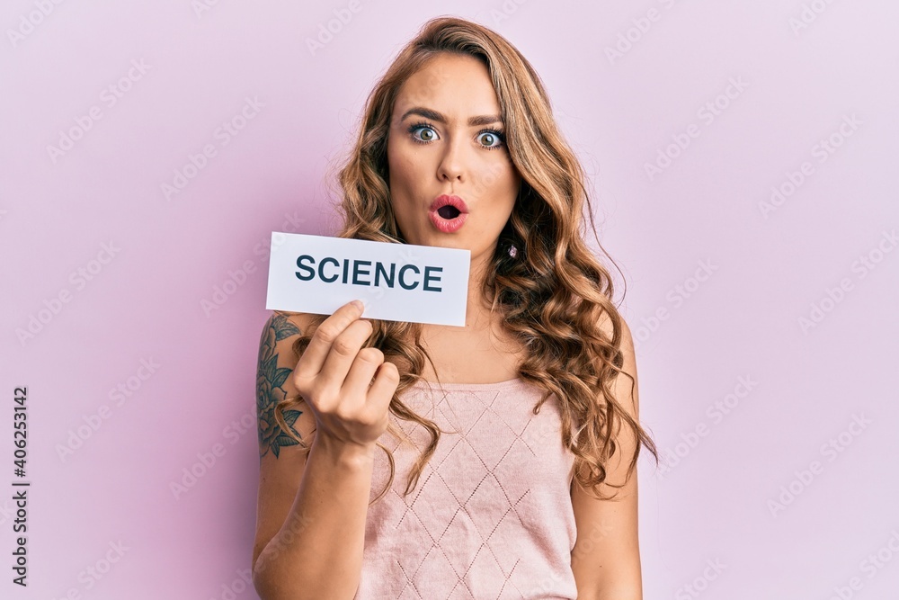 Young blonde girl holding paper with science message scared and amazed with open mouth for surprise, disbelief face Young blonde girl holding paper with science message scared and amazed with open mouth for surprise, disbelief face