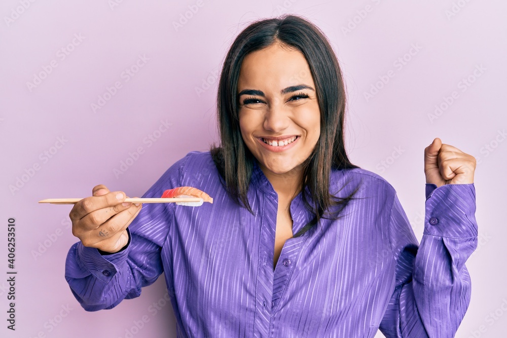 Young brunette woman eating sushi using chopsticks screaming proud, celebrating victory and success very excited with raised arm Young brunette woman eating sushi using chopsticks screaming proud, celebrating victory and success very excited with raised arm