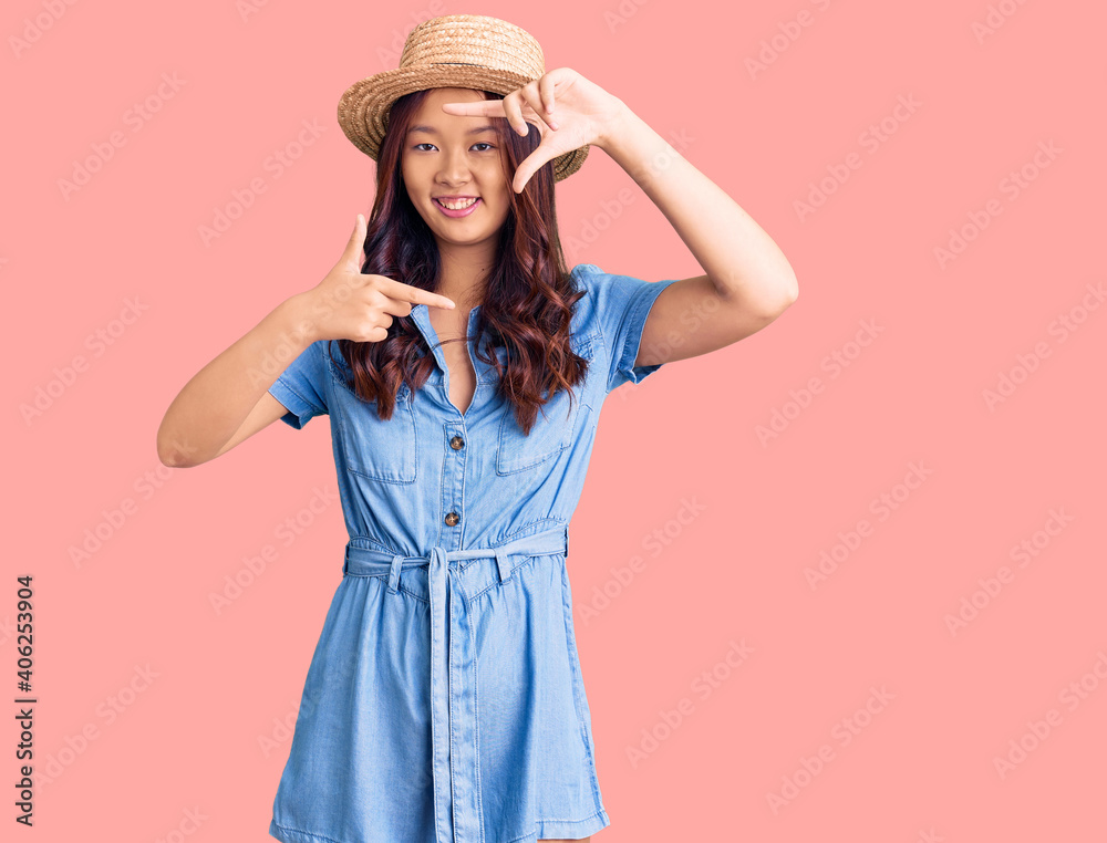 Young beautiful chinese girl wearing summer hat smiling making frame with hands and fingers with happy face. creativity and photography concept. Young beautiful chinese girl wearing summer hat smiling making frame with hands and fingers with happy face. creativity and photography concept.