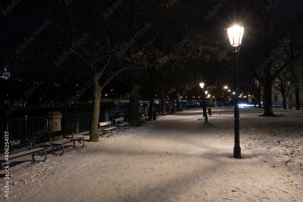 .light from street lights and a walkway sunken with snow in the center of Prague in the park at night