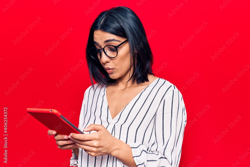 Young beautiful latin woman holding touchpad scared and amazed with open mouth for surprise, disbelief face Young beautiful latin woman holding touchpad scared and amazed with open mouth for surprise, disbelief face