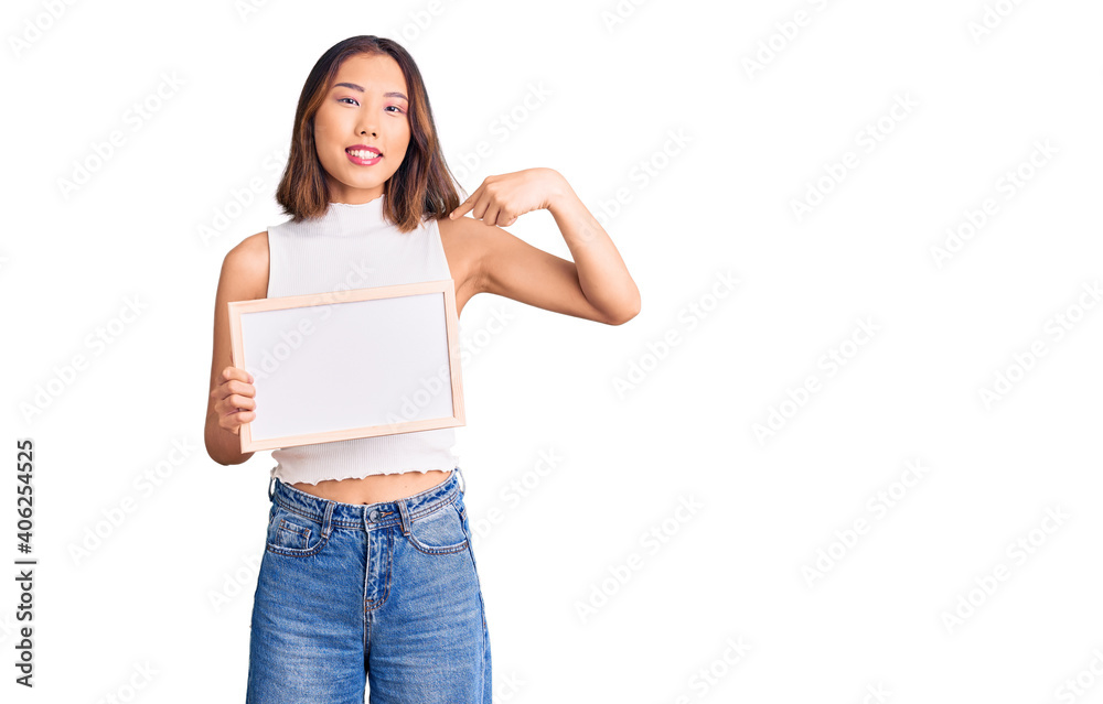 Young beautiful chinese girl holding empty white chalkboard pointing finger to one self smiling happy and proud Young beautiful chinese girl holding empty white chalkboard pointing finger to one self smiling happy and proud