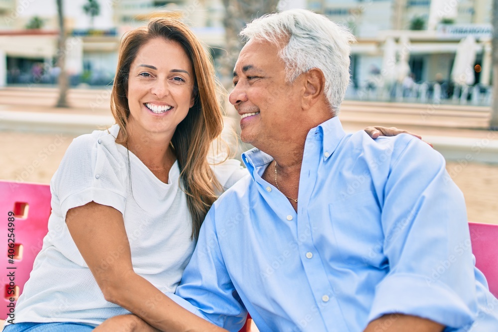Middle age hispanic couple smiling happy and hugging sitting on bench at the beach. Middle age hispanic couple smiling happy and hugging sitting on bench at the beach.