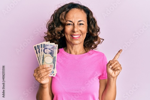 Middle age hispanic woman holding japanese yen banknotes smiling happy pointing with hand and finger to the side
