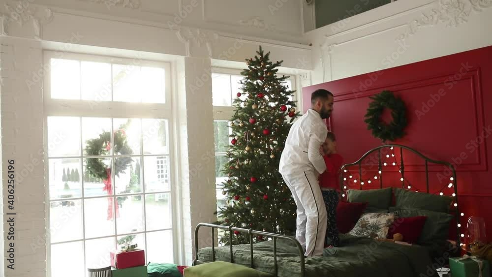Male generations, dad throws his son in the air standing on bed near christmas tree, happy family xmas holidays concept. High quality HD footage