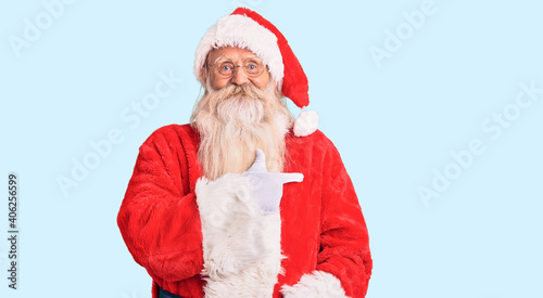 Old senior man with grey hair and long beard wearing traditional santa claus costume cheerful with a smile on face pointing with hand and finger up to the side with happy and natural expression