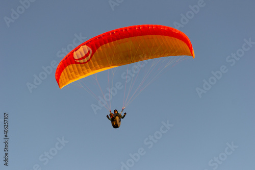 A beautiful view of a paraglide flying gliding on a clear blue sky at the golden hour with a nice wind windy breeze on a sunny day 