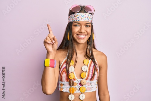 Beautiful hispanic woman wearing bohemian and hippie style showing and pointing up with finger number one while smiling confident and happy.