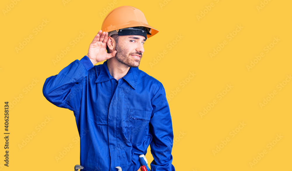Young hispanic man wearing worker uniform smiling with hand over ear listening an hearing to rumor or gossip. deafness concept.