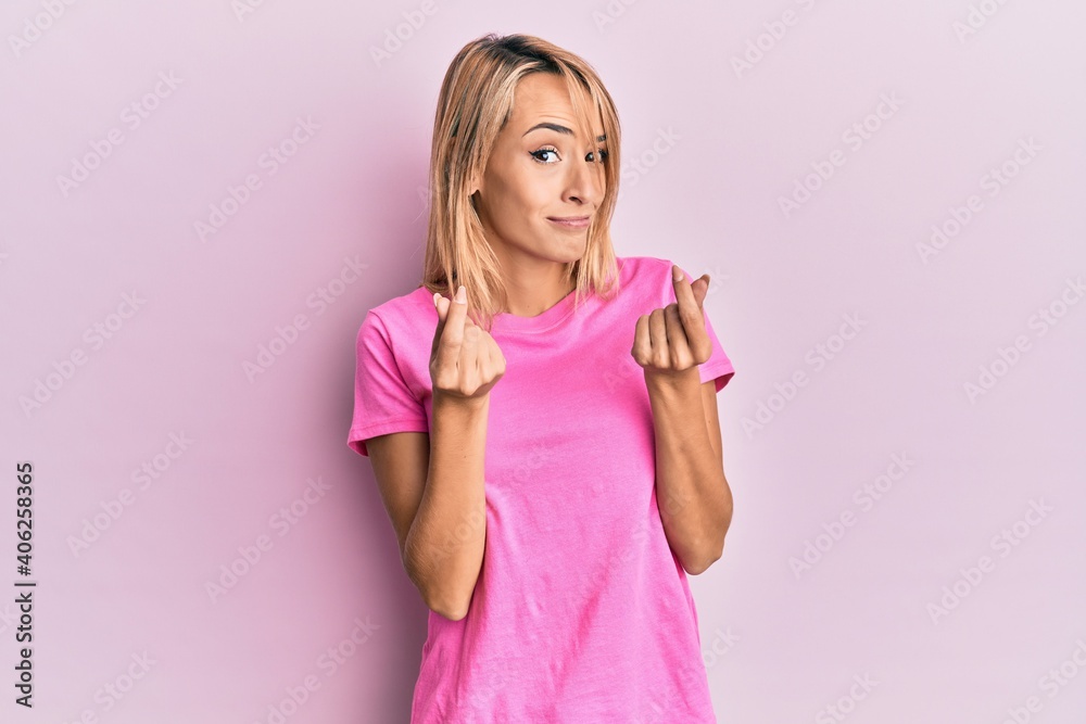 Beautiful blonde woman wearing casual pink tshirt doing money gesture with hands, asking for salary payment, millionaire business Beautiful blonde woman wearing casual pink tshirt doing money gesture with hands, asking for salary payment, millionaire business