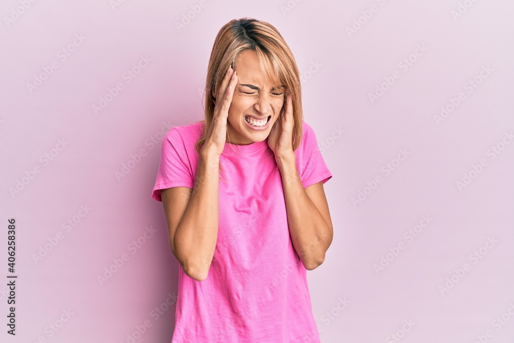 Beautiful blonde woman wearing casual pink tshirt with hand on head, headache because stress. suffering migraine. Beautiful blonde woman wearing casual pink tshirt with hand on head, headache because stress. suffering migraine.