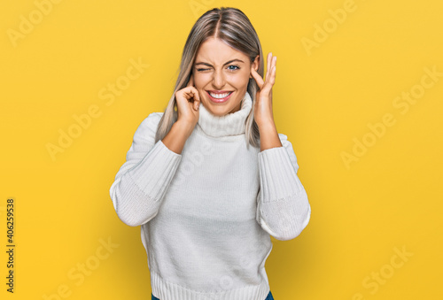 Beautiful blonde woman wearing casual turtleneck sweater covering ears with fingers with annoyed expression for the noise of loud music. deaf concept.