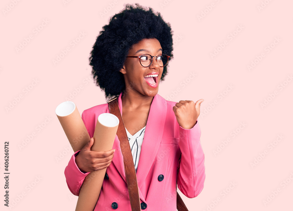 Young african american woman holding architect blueprints pointing thumb up to the side smiling happy with open mouth Young african american woman holding architect blueprints pointing thumb up to the side smiling happy with open mouth