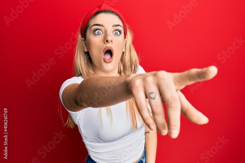 Young caucasian woman wearing casual white t shirt pointing with finger surprised ahead, open mouth amazed expression, something on the front