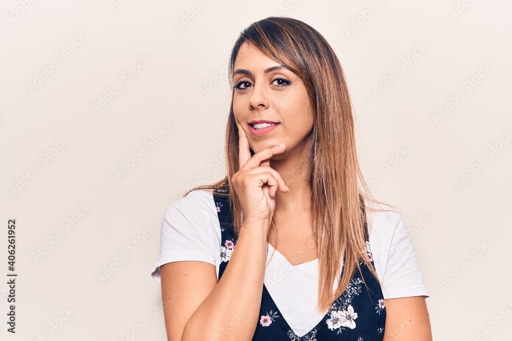 Young beautiful woman wearing casual floral dress smiling looking confident at the camera with crossed arms and hand on chin. thinking positive. Young beautiful woman wearing casual floral dress smiling looking confident at the camera with crossed arms and hand on chin. thinking positive.