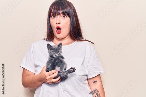 Young plus size woman holding cat scared and amazed with open mouth for surprise  disbelief face