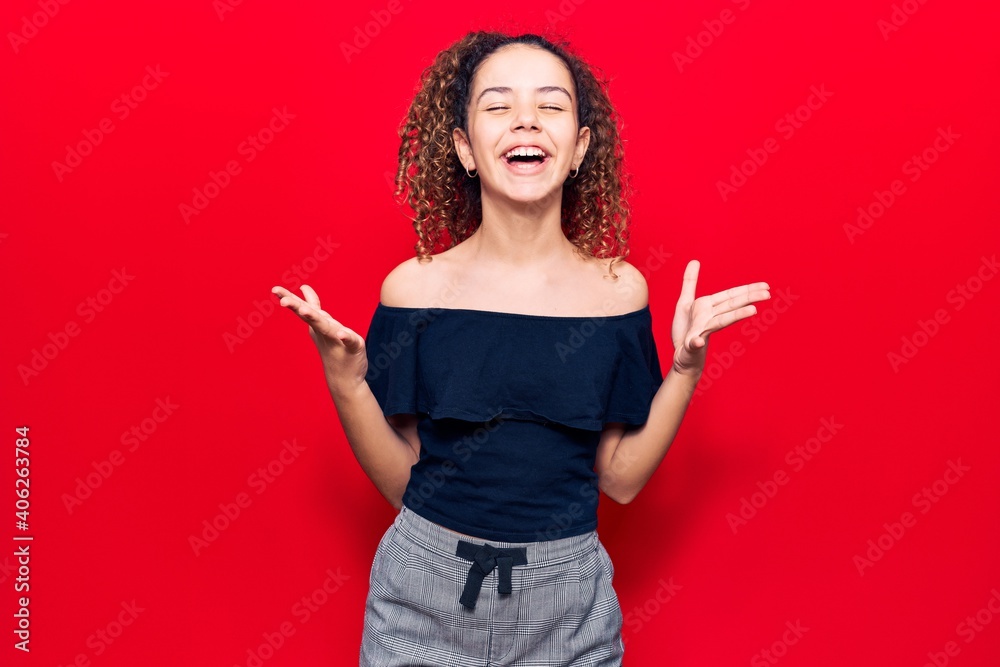 Beautiful kid girl with curly hair wearing casual clothes celebrating mad and crazy for success with arms raised and closed eyes screaming excited. winner concept Beautiful kid girl with curly hair wearing casual clothes celebrating mad and crazy for success with arms raised and closed eyes screaming excited. winner concept