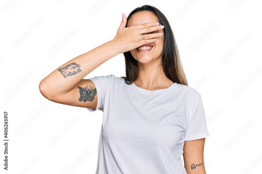 Young hispanic woman wearing casual white t shirt smiling and laughing with hand on face covering eyes for surprise. blind concept. Young hispanic woman wearing casual white t shirt smiling and laughing with hand on face covering eyes for surprise. blind concept.