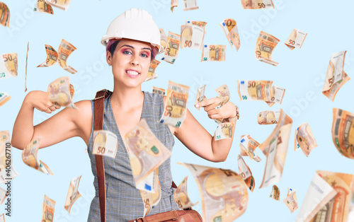 Young beautiful woman wearing architect hardhat and leather bag looking confident with smile on face, pointing oneself with fingers proud and happy.