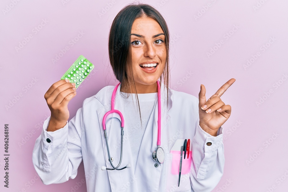 Beautiful hispanic woman wearing doctor uniform holding prescription pills smiling happy pointing with hand and finger to the side Beautiful hispanic woman wearing doctor uniform holding prescription pills smiling happy pointing with hand and finger to the side