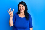 Plus size brunette woman wearing casual blue shirt showing and pointing up with fingers number four while smiling confident and happy.
