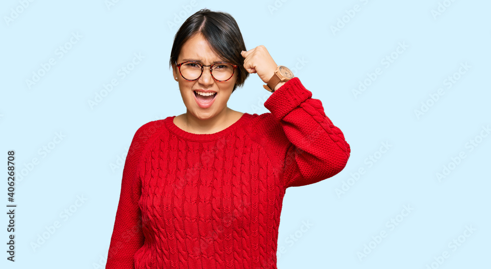 Young beautiful hispanic woman with short hair wearing casual sweater and glasses angry and mad raising fist frustrated and furious while shouting with anger. rage and aggressive concept. Young beautiful hispanic woman with short hair wearing casual sweater and glasses angry and mad raising fist frustrated and furious while shouting with anger. rage and aggressive concept.