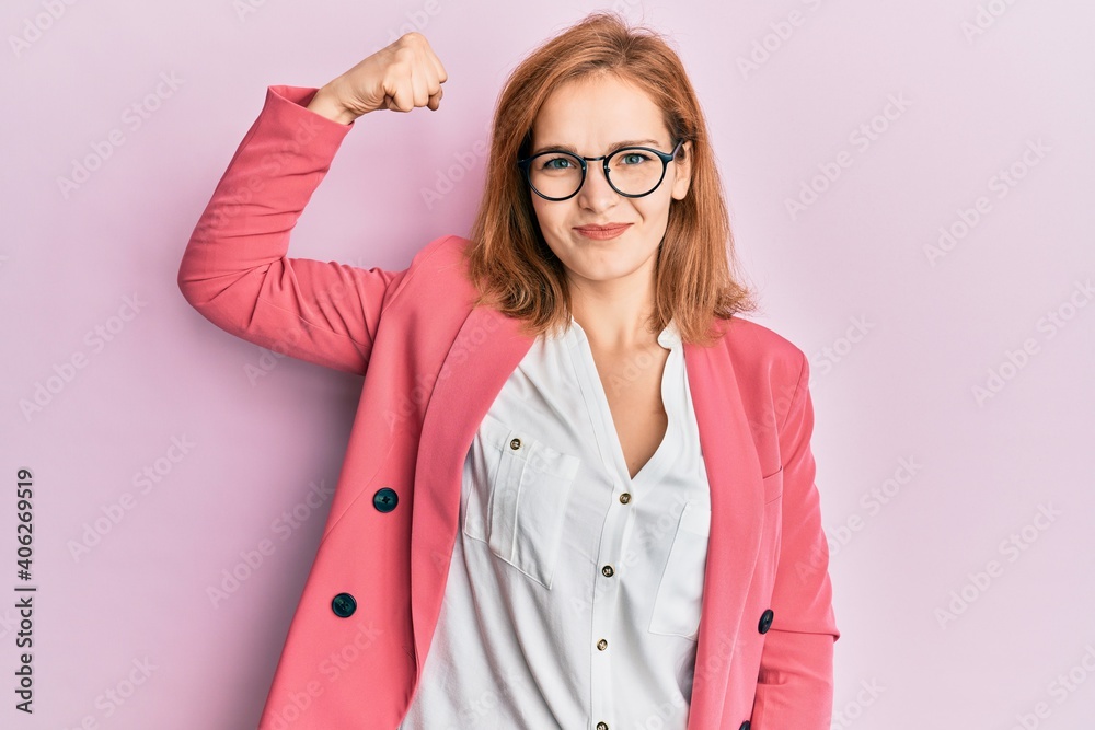 Young caucasian woman wearing business style and glasses strong person showing arm muscle, confident and proud of power