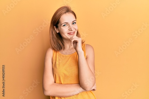 Young caucasian woman wearing casual style with sleeveless shirt looking confident at the camera with smile with crossed arms and hand raised on chin. thinking positive.