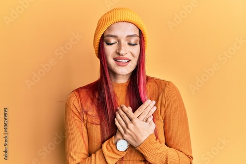 Young caucasian woman wearing wool cap smiling with hands on chest with closed eyes and grateful gesture on face. health concept. © Krakenimages.com