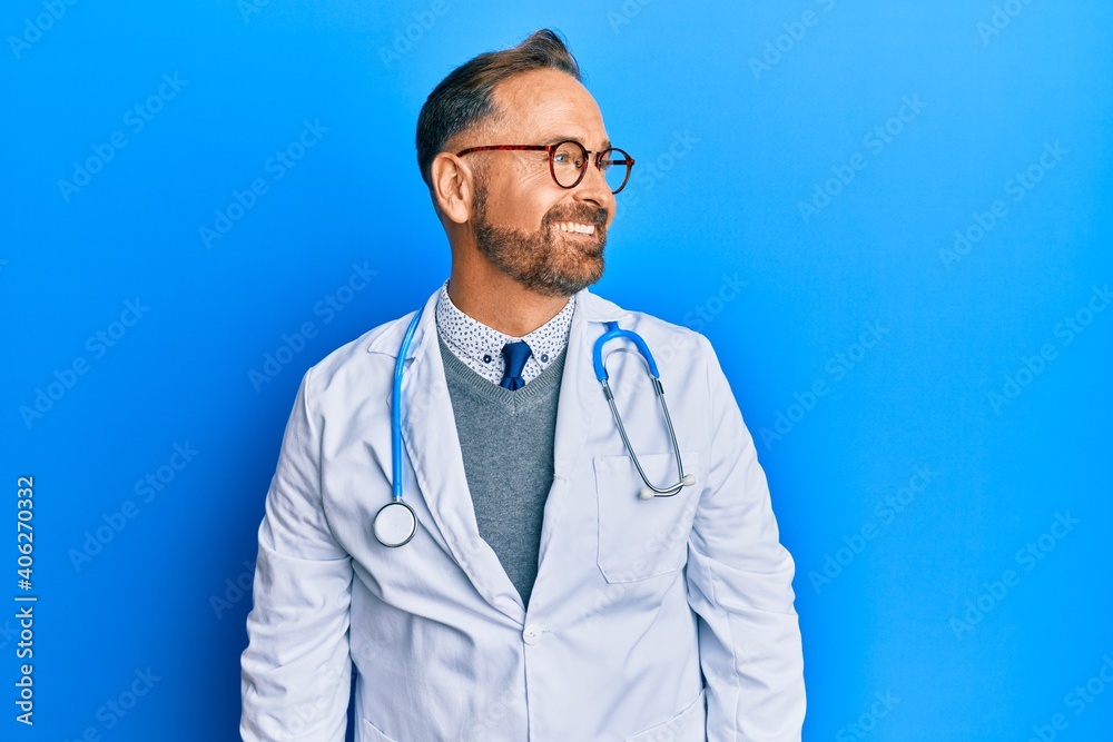 Handsome middle age man wearing doctor uniform and stethoscope looking away to side with smile on face, natural expression. laughing confident. Handsome middle age man wearing doctor uniform and stethoscope looking away to side with smile on face, natural expression. laughing confident.