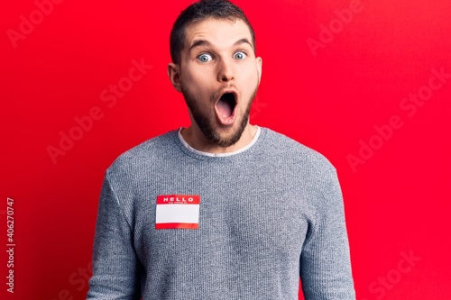 фотографія Young handsome man wearing hello my name is sticker scared and amazed with open