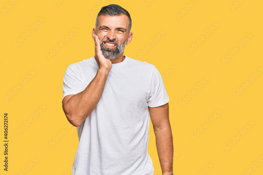 Middle age handsome man wearing casual white tshirt touching mouth with hand with painful expression because of toothache or dental illness on teeth. dentist Middle age handsome man wearing casual white tshirt touching mouth with hand with painful expression because of toothache or dental illness on teeth. dentist