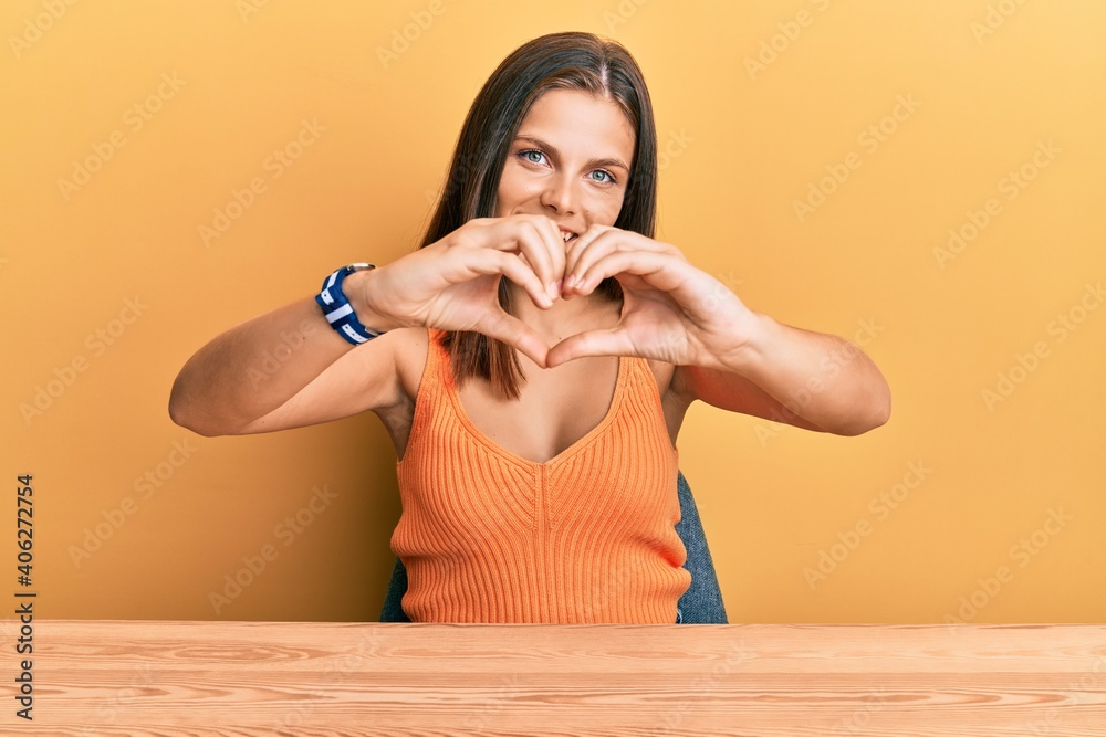 Young caucasian woman wearing casual clothes sitting on the table smiling in love doing heart symbol shape with hands. romantic concept. Young caucasian woman wearing casual clothes sitting on the table smiling in love doing heart symbol shape with hands. romantic concept.