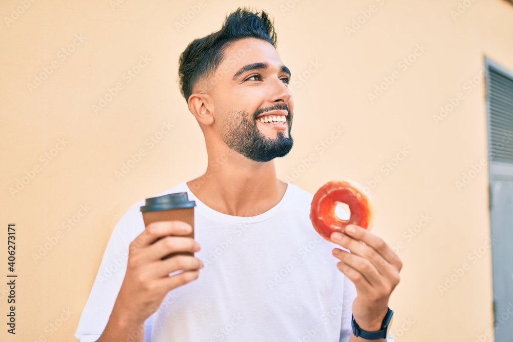 Young arab man smiling happy eating donut and drinking coffee at the city. Young arab man smiling happy eating donut and drinking coffee at the city.