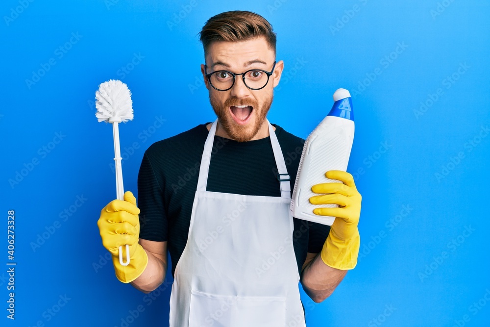 Young redhead man doing bathroom housework with toilet brush celebrating crazy and amazed for success with open eyes screaming excited. Young redhead man doing bathroom housework with toilet brush celebrating crazy and amazed for success with open eyes screaming excited.