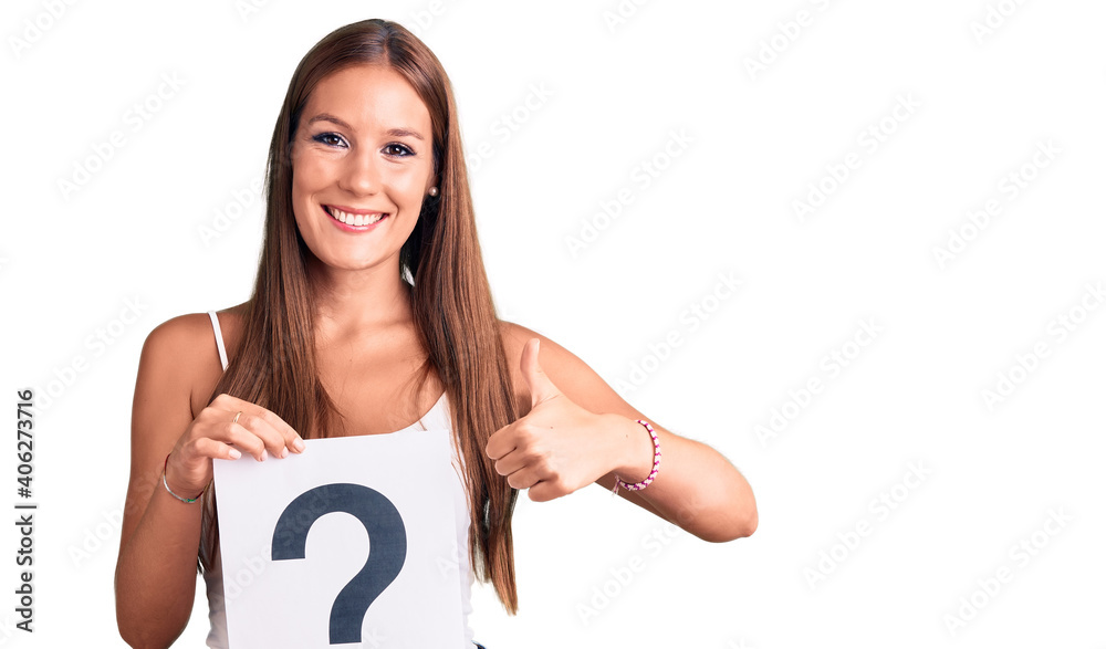 Young beautiful hispanic woman holding question mark smiling happy and positive, thumb up doing excellent and approval sign Young beautiful hispanic woman holding question mark smiling happy and positive, thumb up doing excellent and approval sign