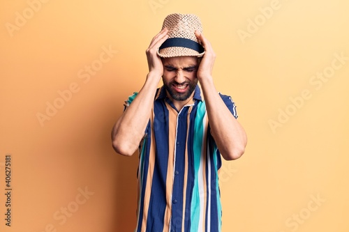 Young handsome man with beard wearing summer hat and shirt suffering from headache desperate and stressed because pain and migraine. hands on head.