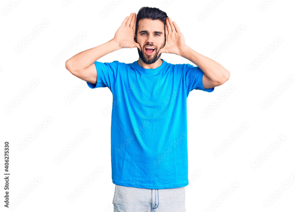 Young handsome man with beard wearing casual t-shirt smiling cheerful playing peek a boo with hands showing face. surprised and exited Young handsome man with beard wearing casual t-shirt smiling cheerful playing peek a boo with hands showing face. surprised and exited