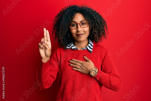 Beautiful african american woman with afro hair wearing sweater and glasses smiling swearing with hand on chest and fingers up, making a loyalty promise oath