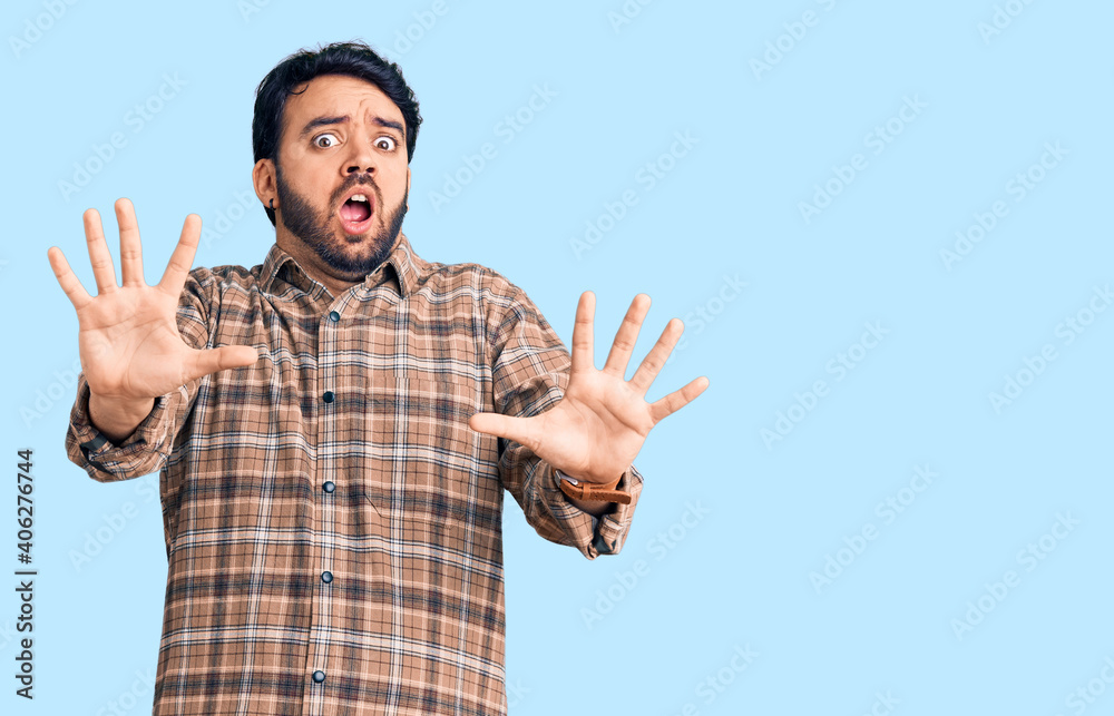 Young hispanic man wearing casual clothes afraid and terrified with fear expression stop gesture with hands, shouting in shock. panic concept. Young hispanic man wearing casual clothes afraid and terrified with fear expression stop gesture with hands, shouting in shock. panic concept.