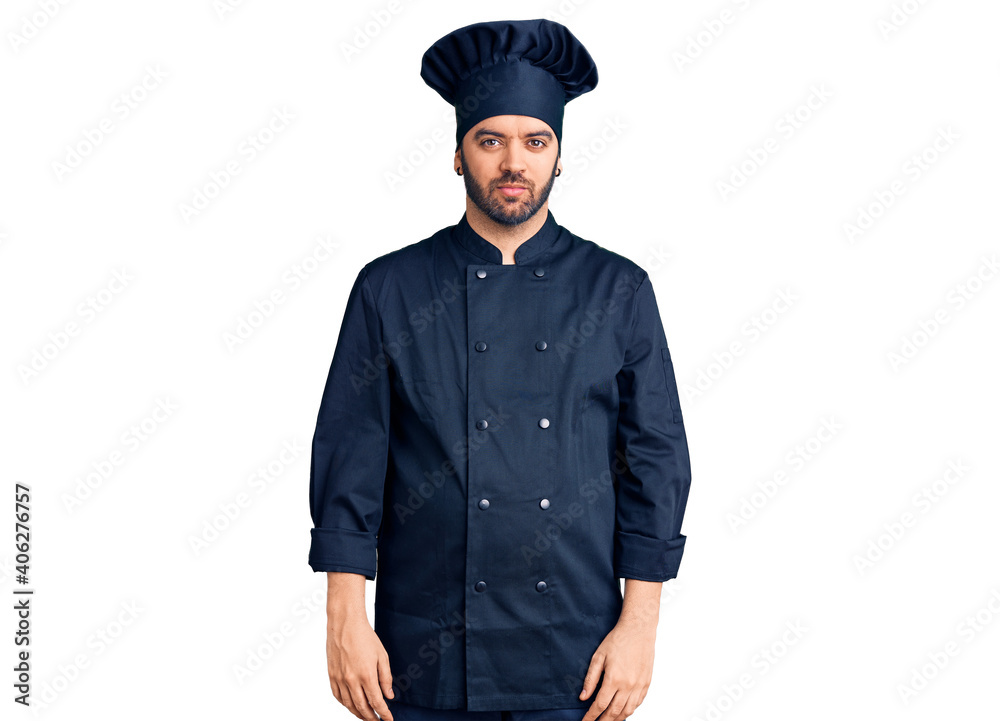 Young hispanic man wearing cooker uniform relaxed with serious expression on face. simple and natural looking at the camera. Young hispanic man wearing cooker uniform relaxed with serious expression on face. simple and natural looking at the camera.