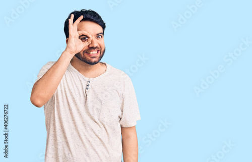 Young hispanic man wearing casual clothes doing ok gesture with hand smiling, eye looking through fingers with happy face. © Krakenimages.com