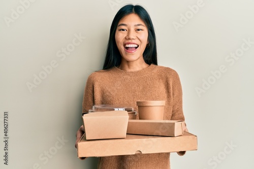 Young chinese woman holding take away food smiling and laughing hard out loud because funny crazy joke.