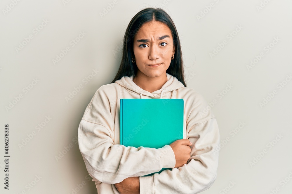 Young asian woman holding book skeptic and nervous, frowning upset because of problem. negative person. Young asian woman holding book skeptic and nervous, frowning upset because of problem. negative person.