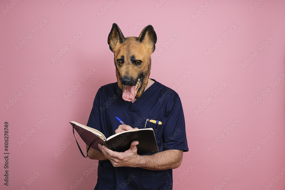 Young man in a latex dog head mask taking some notes on a pink background - obrazy, fototapety, plakaty 