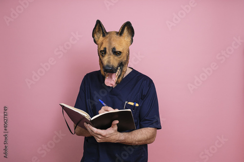 Young man in a latex dog head mask taking some notes on a pink background