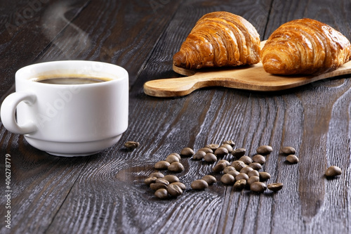 A cup of hot coffee and croissants on a wooden background. Breakfast with coffee and fresh pastry. Copy space. Fresh cake and pastry